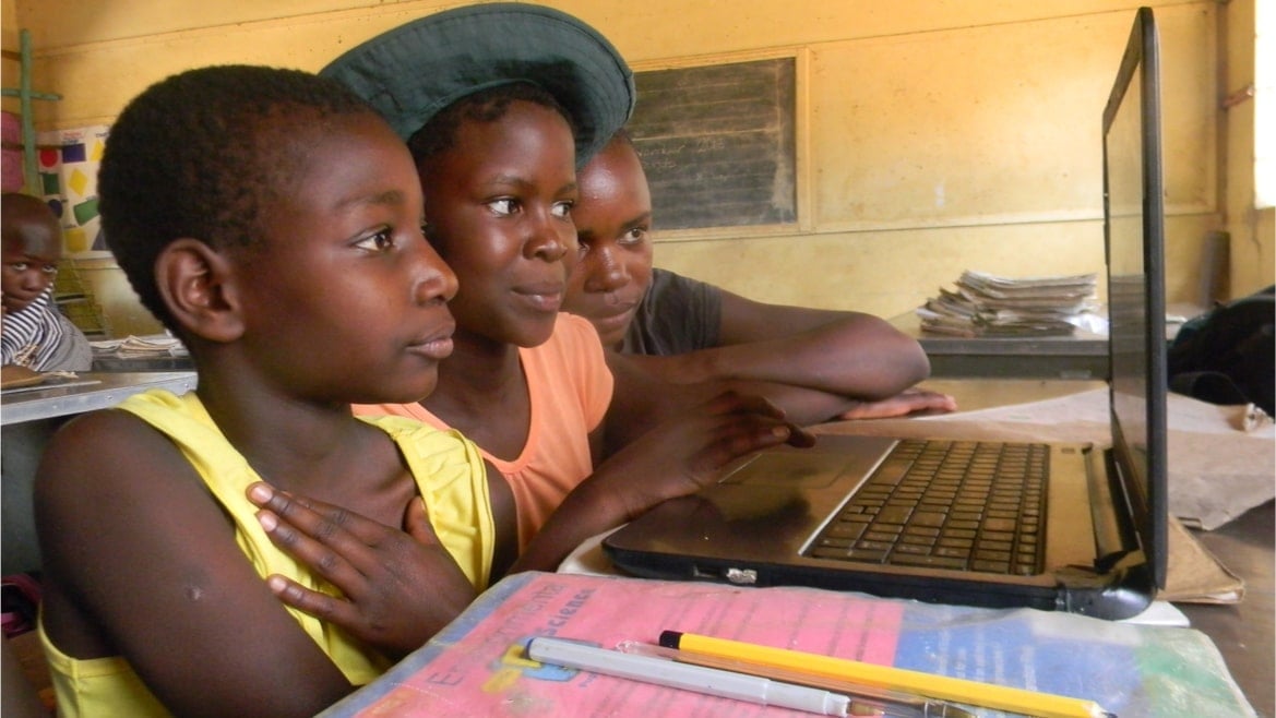 Three high school students in Zimbabwe working on a laptop.