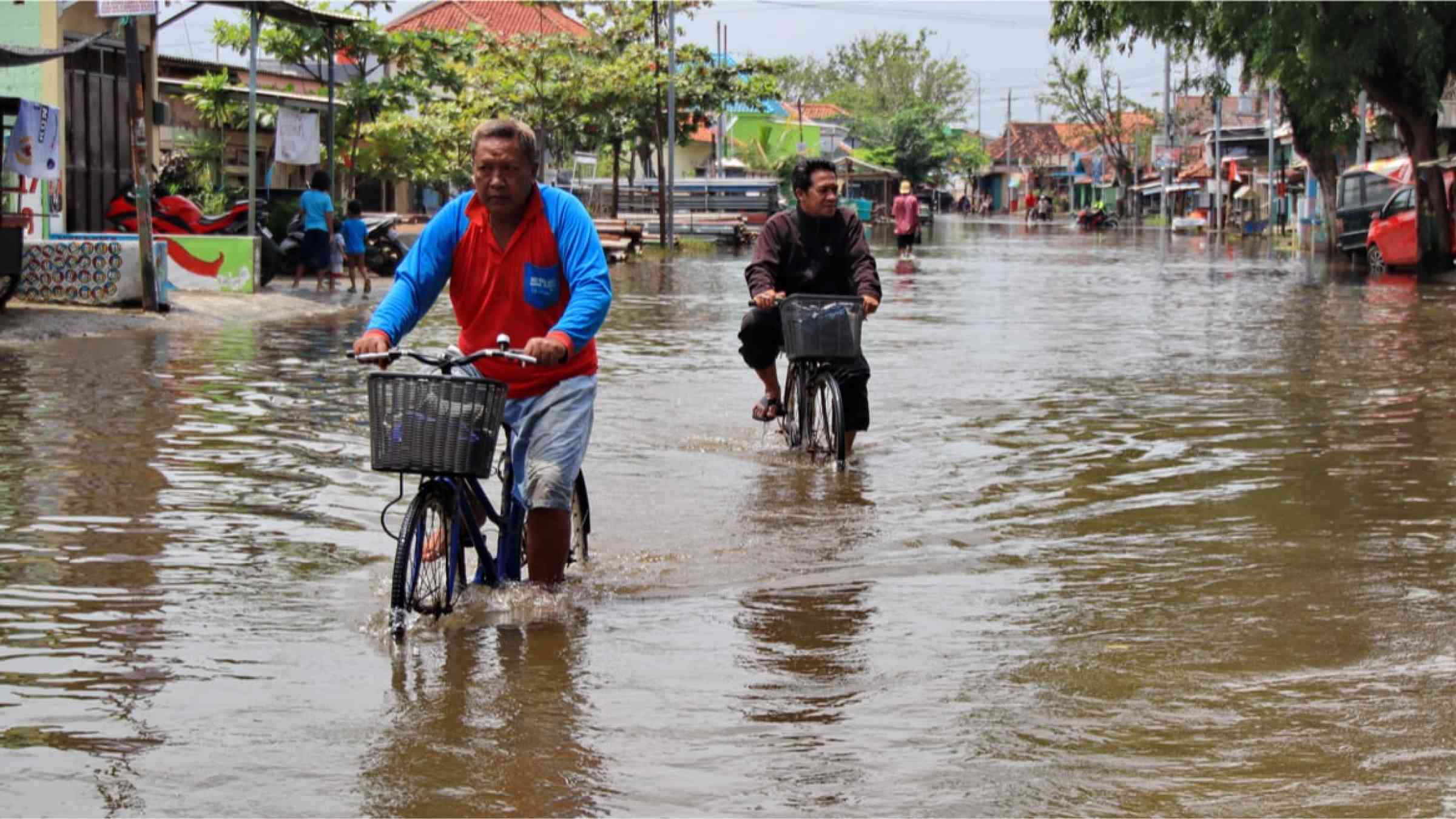 Cyclists driving through flooded streets in Pekalongan, Indonesia (2021)
