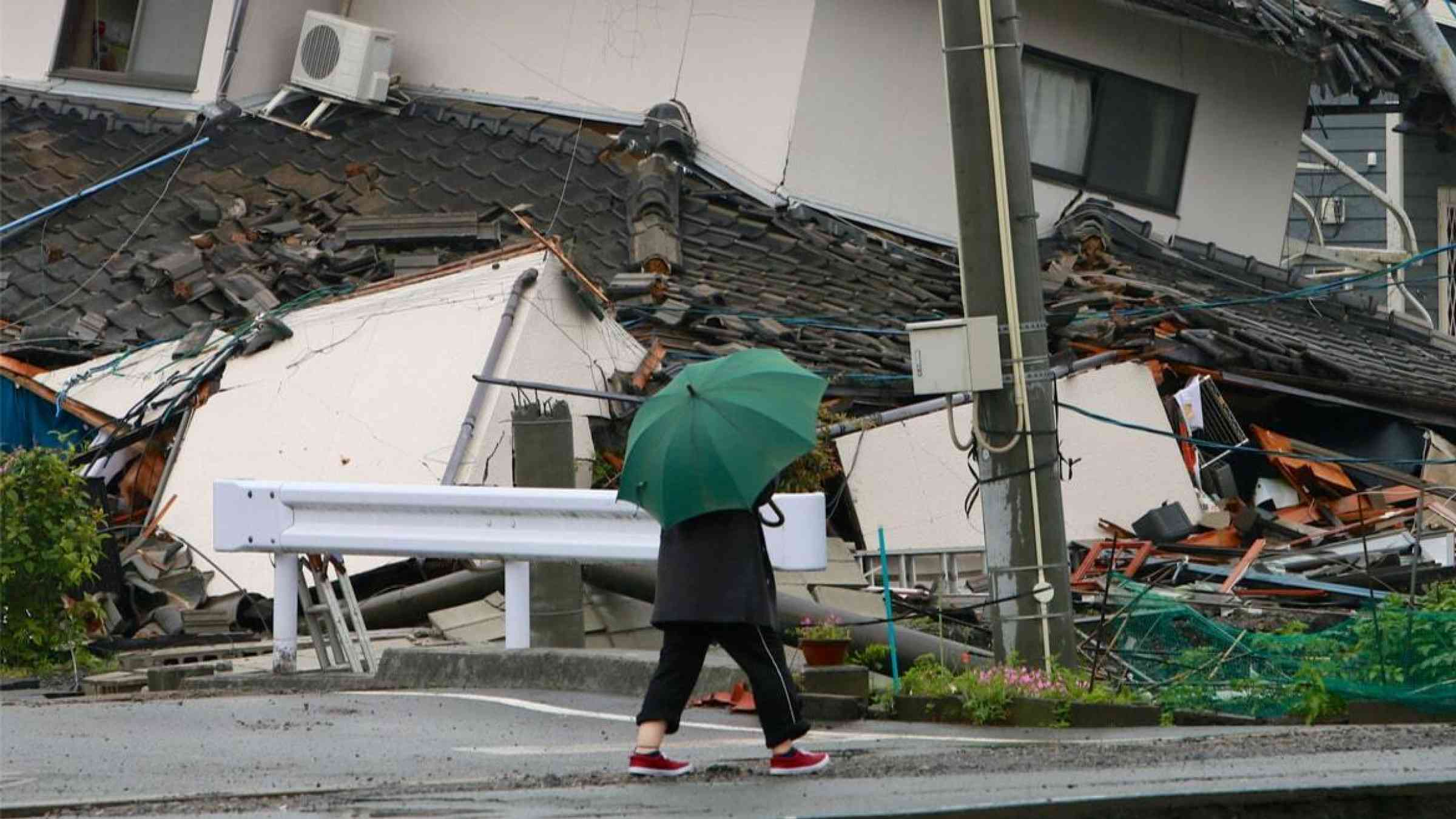 A resident walks past a collapsed house in the aftermath of the 2011 Tōhoku earthquake