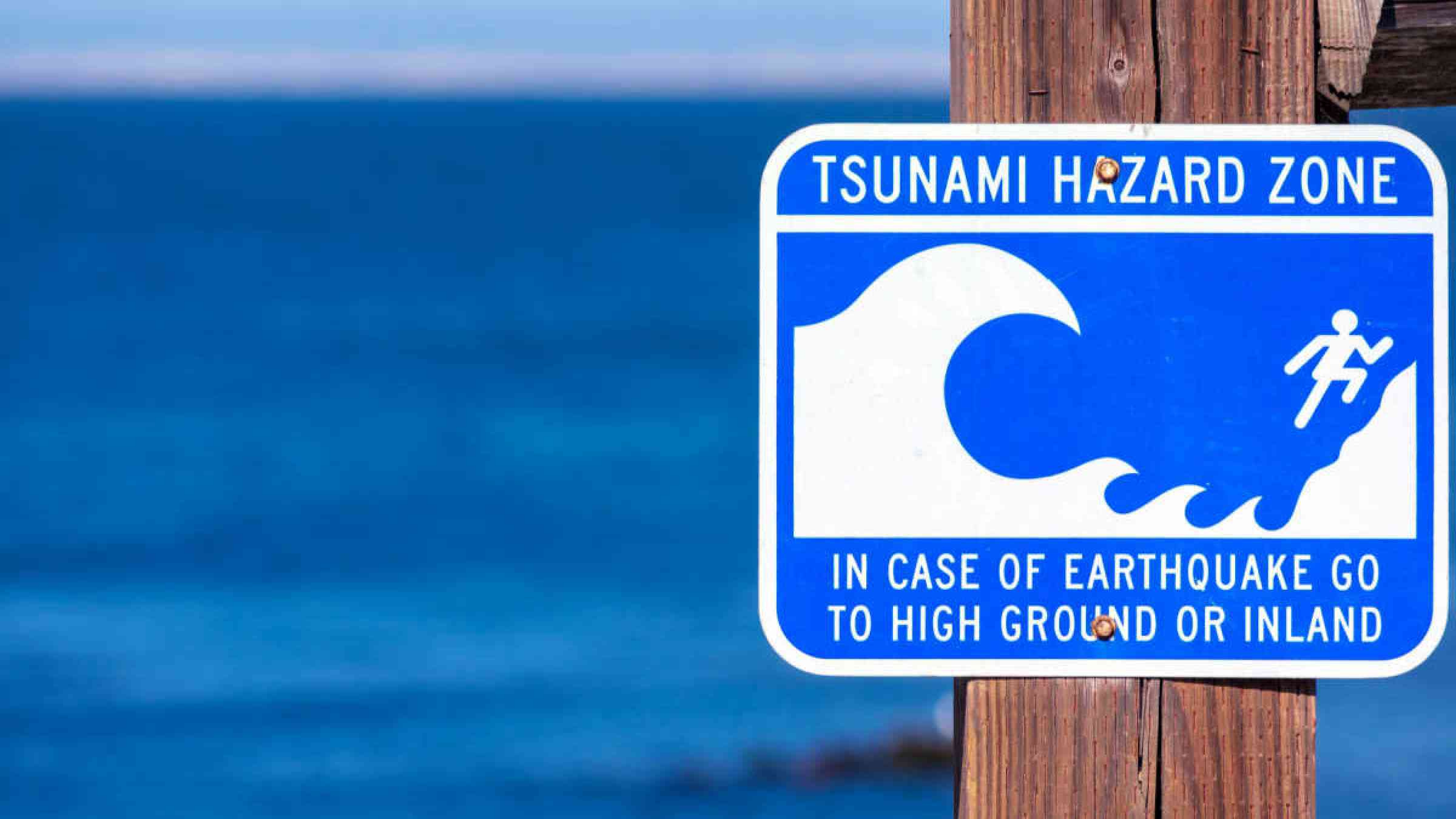 Tsunami Hazard Zone warning sign on the Pacific Ocean coast warn the public about possible danger after an earthquake. Blurred blue ocean surface on horizon